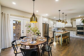 Une cuisine moderne avec des meubles blancs, des appareils en acier inoxydable et une table à manger en bois pour quatre personnes.