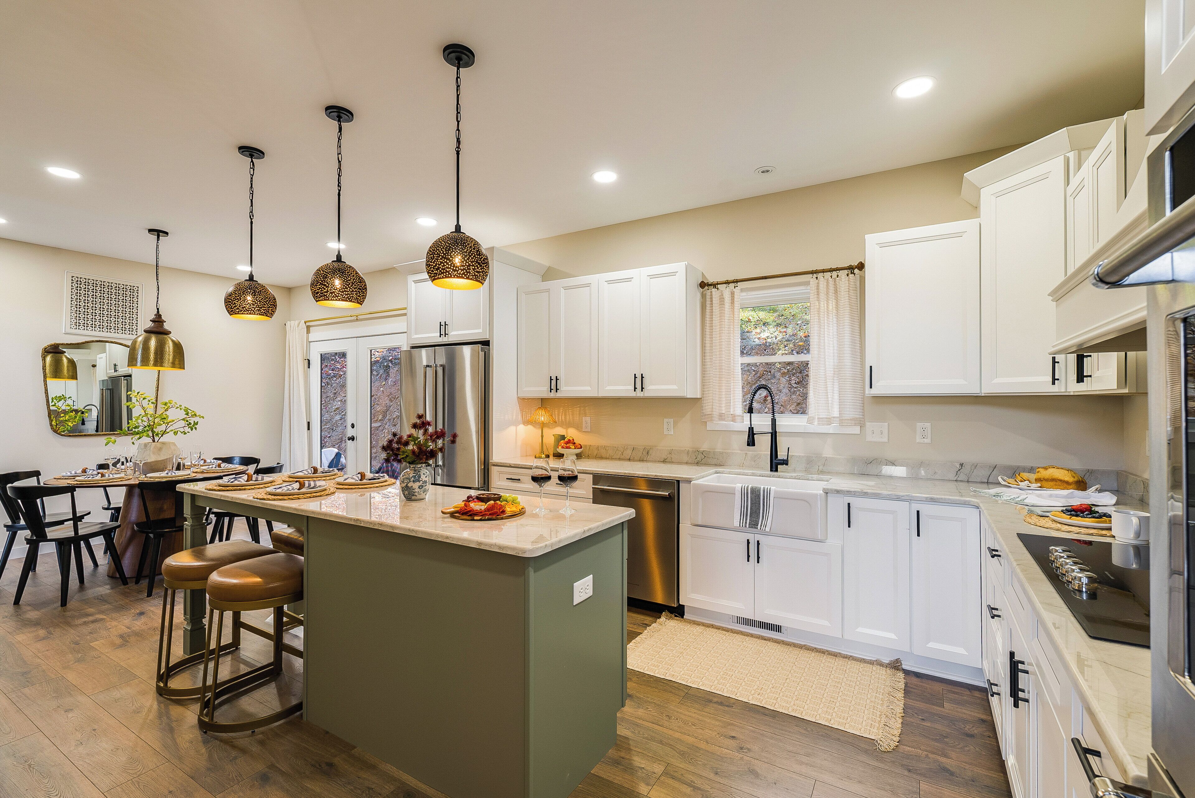 A modern kitchen with white cabinetry, a central island, stainless steel appliances, pendant lighting, and a dining area with a wooden table and chairs.
