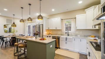 A modern kitchen with white cabinetry, a central island, stainless steel appliances, pendant lighting, and a dining area with a wooden table and chairs.