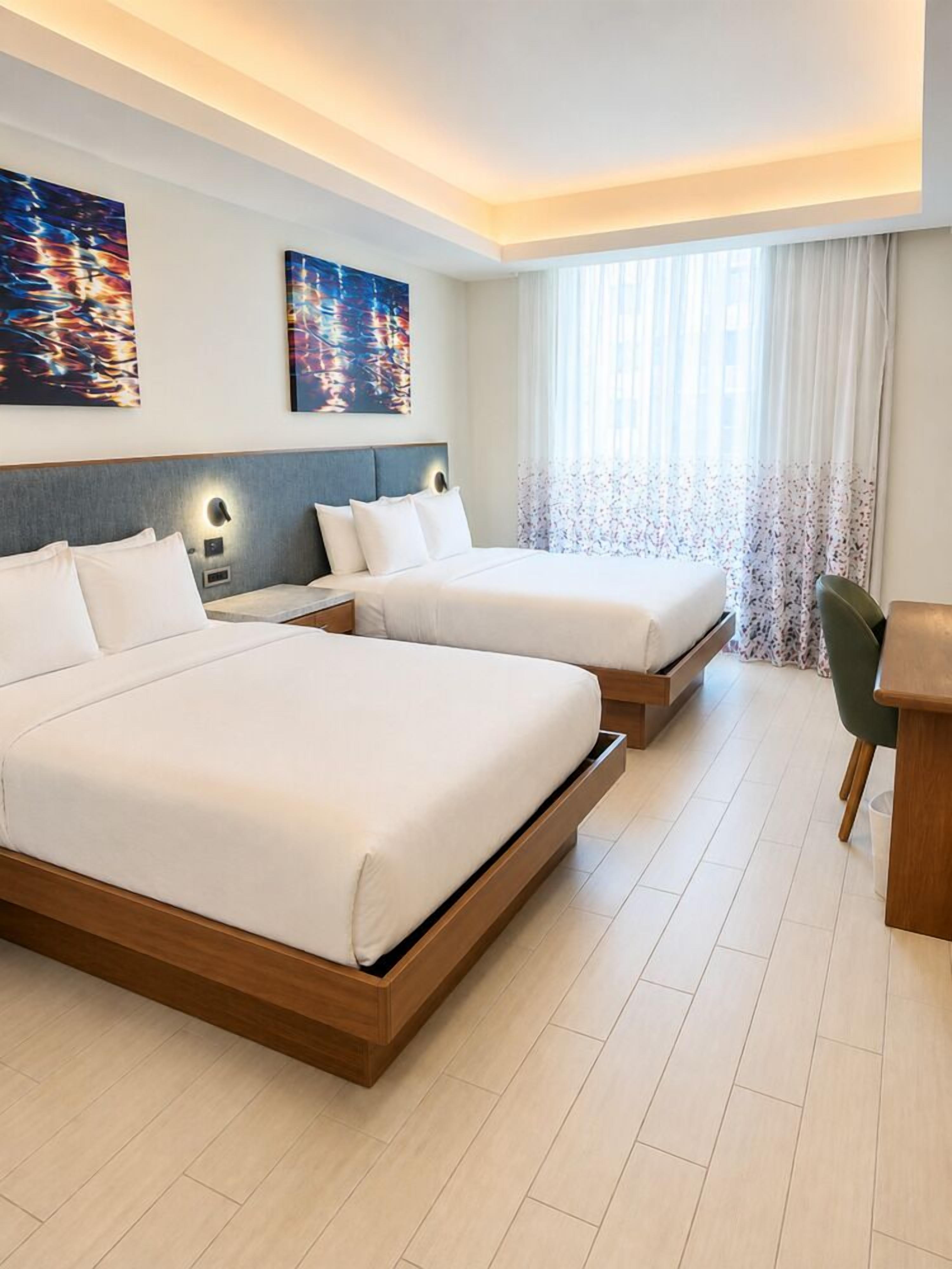 A hotel room with two beds, a desk, and a chair.