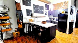 A kitchen with a central island, dark cabinets, and a wooden floor. - Eclectic Loft in Historic Corktown where vibrance meets serenity – 75" TV & KING (Detroit)
