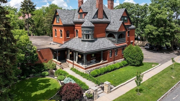 Une grande maison à deux étages, dotée d’une véranda qui fait le tour de la maison, d’une façade en briques et de plusieurs cheminées.