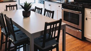 Une cuisine moderne avec des armoires blanches, un îlot central doté de chaises, un four encastré, un four à micro-ondes et un luminaire suspendu.