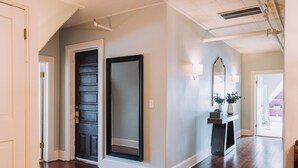Un couloir avec une porte en bois sombre, un grand miroir et une petite console sur laquelle est posé un vase.