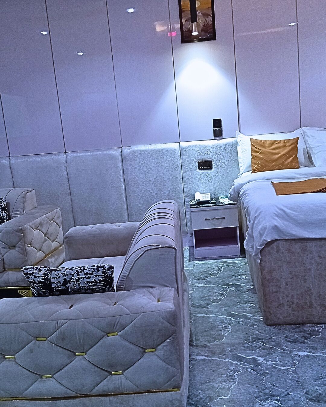 Une chambre d’hôtel moderne avec un grand lit, deux canapés, une petite table et un téléphone fixé au mur.