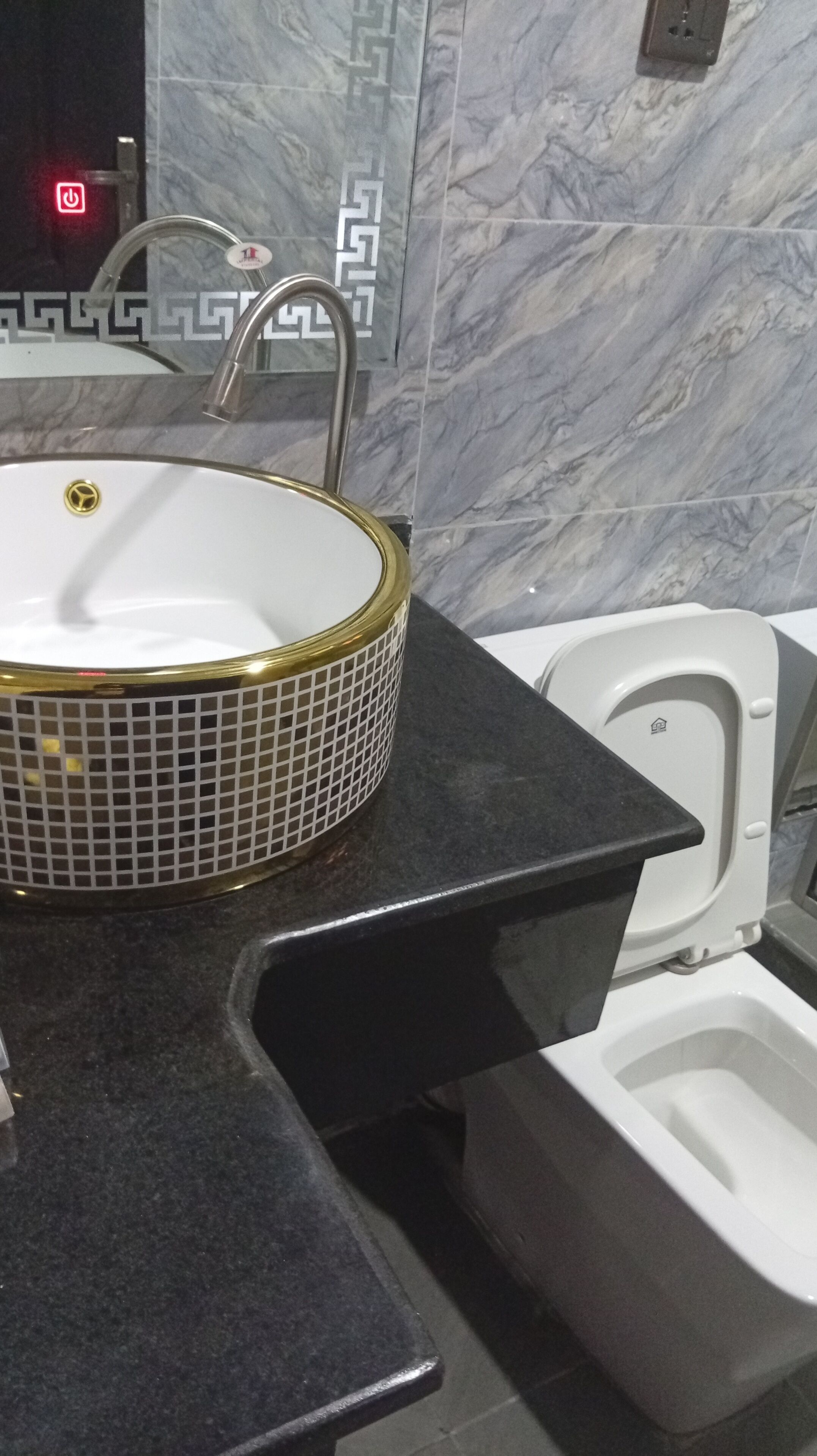 Une salle de bain avec un lavabo blanc orné d’un bord doré, un plan de toilette noir et des toilettes blanches.