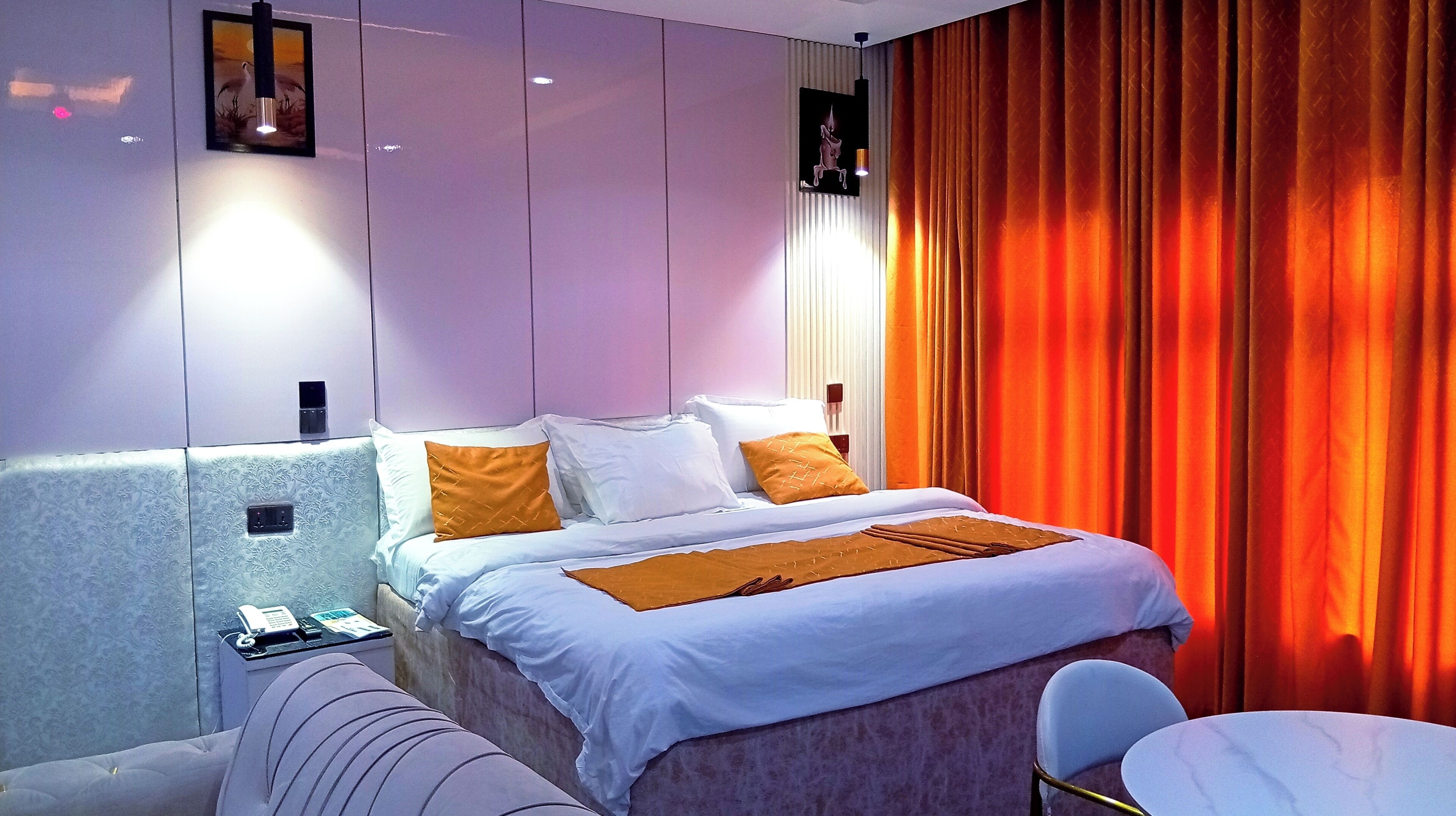 A modern hotel room with a neatly made bed, a bedside table with a phone, and a chair.