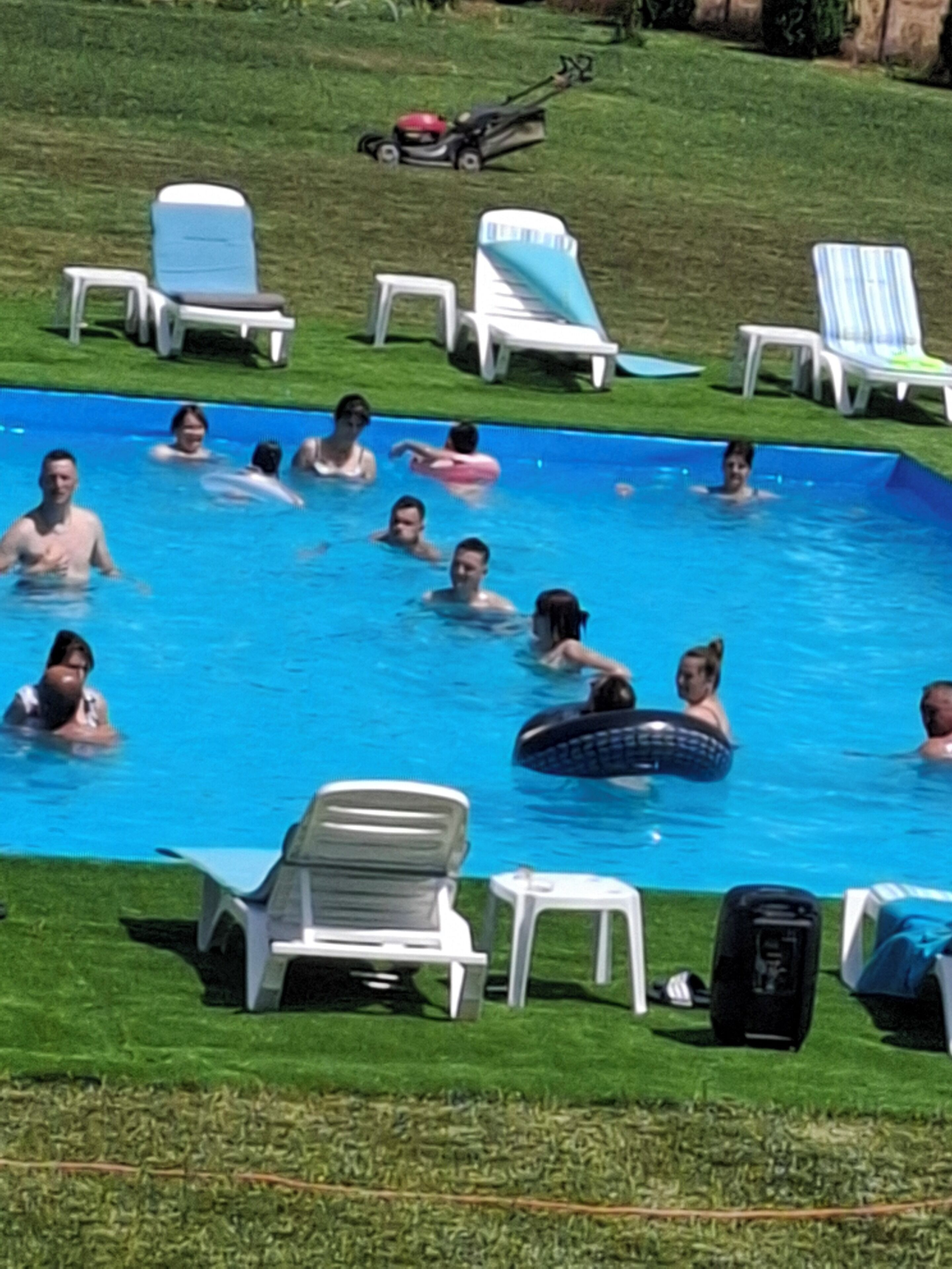 Una piscina con gente y sillones de descanso.
