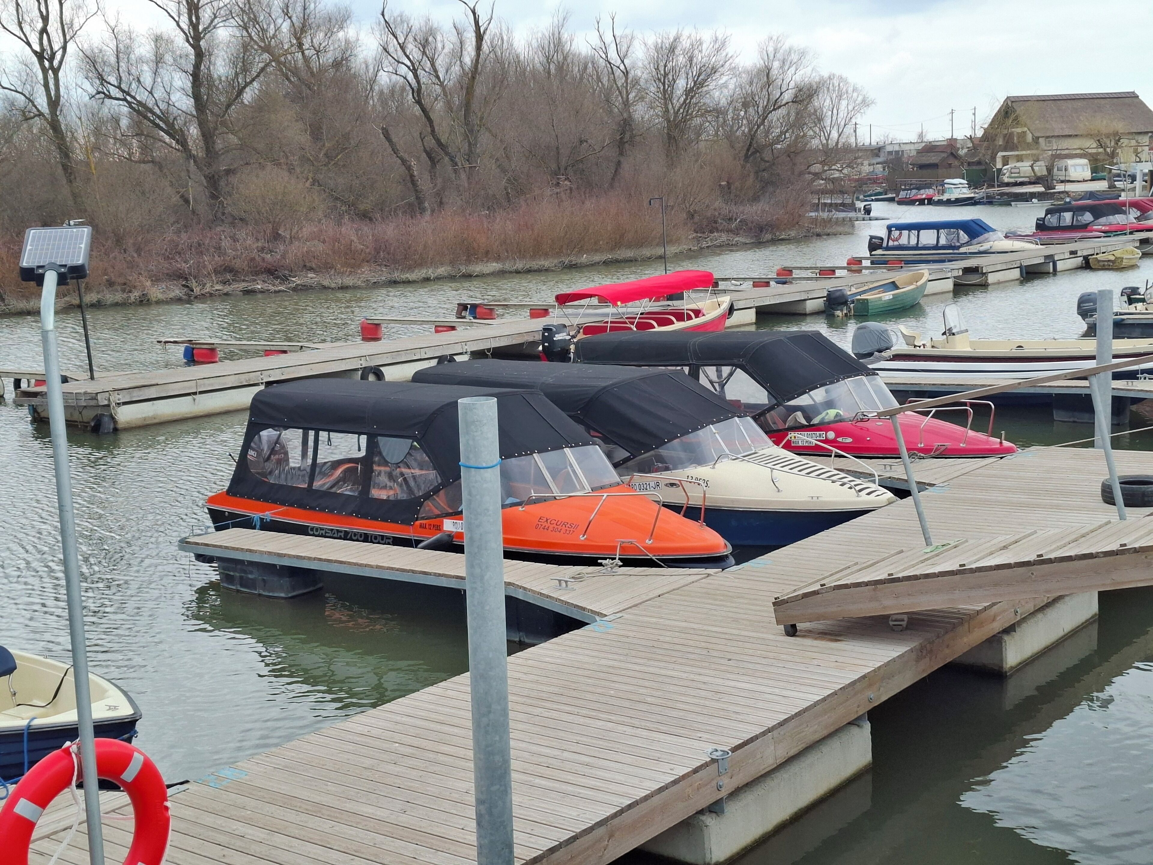 A marina with several boats docked, a wooden pier, and a lifebuoy.