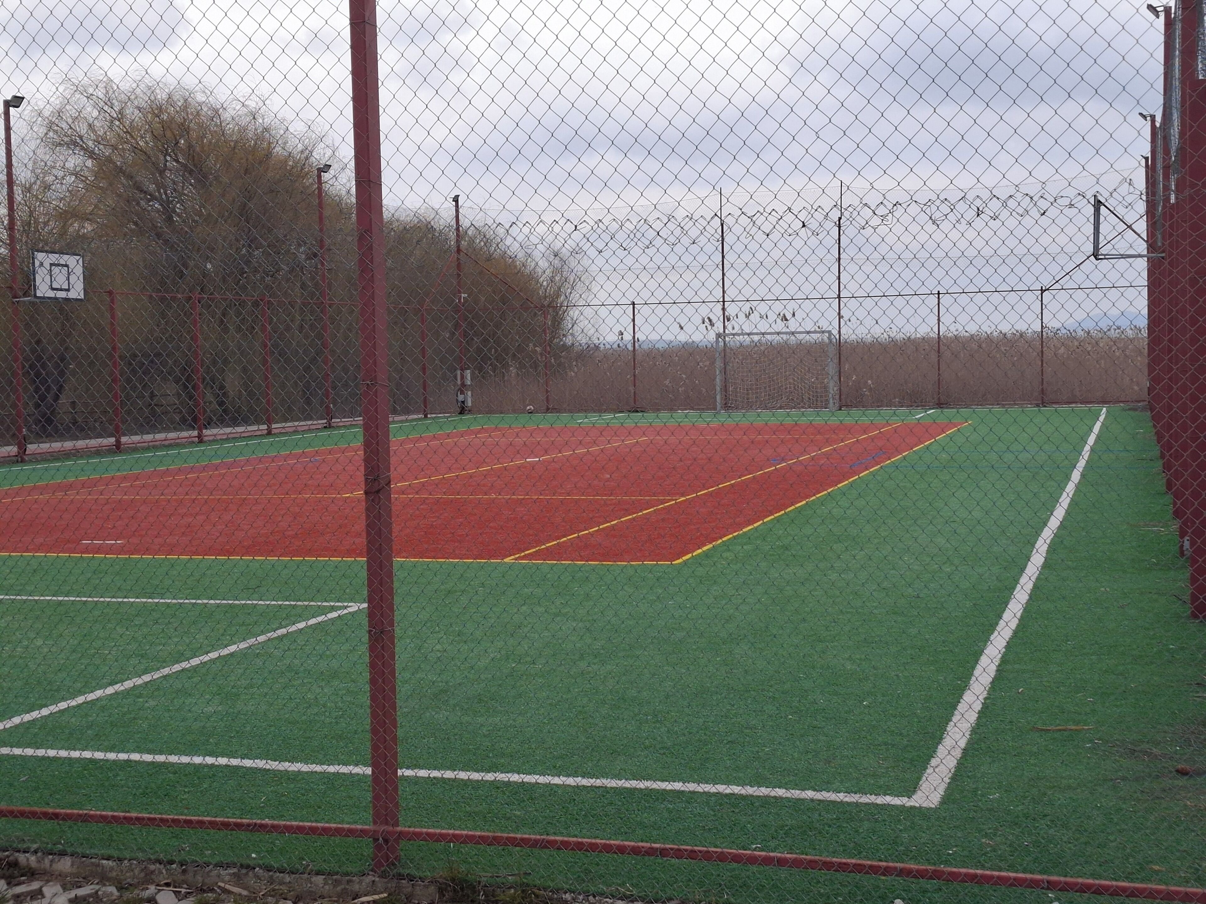 A fenced sports court with a basketball hoop and a soccer goal.