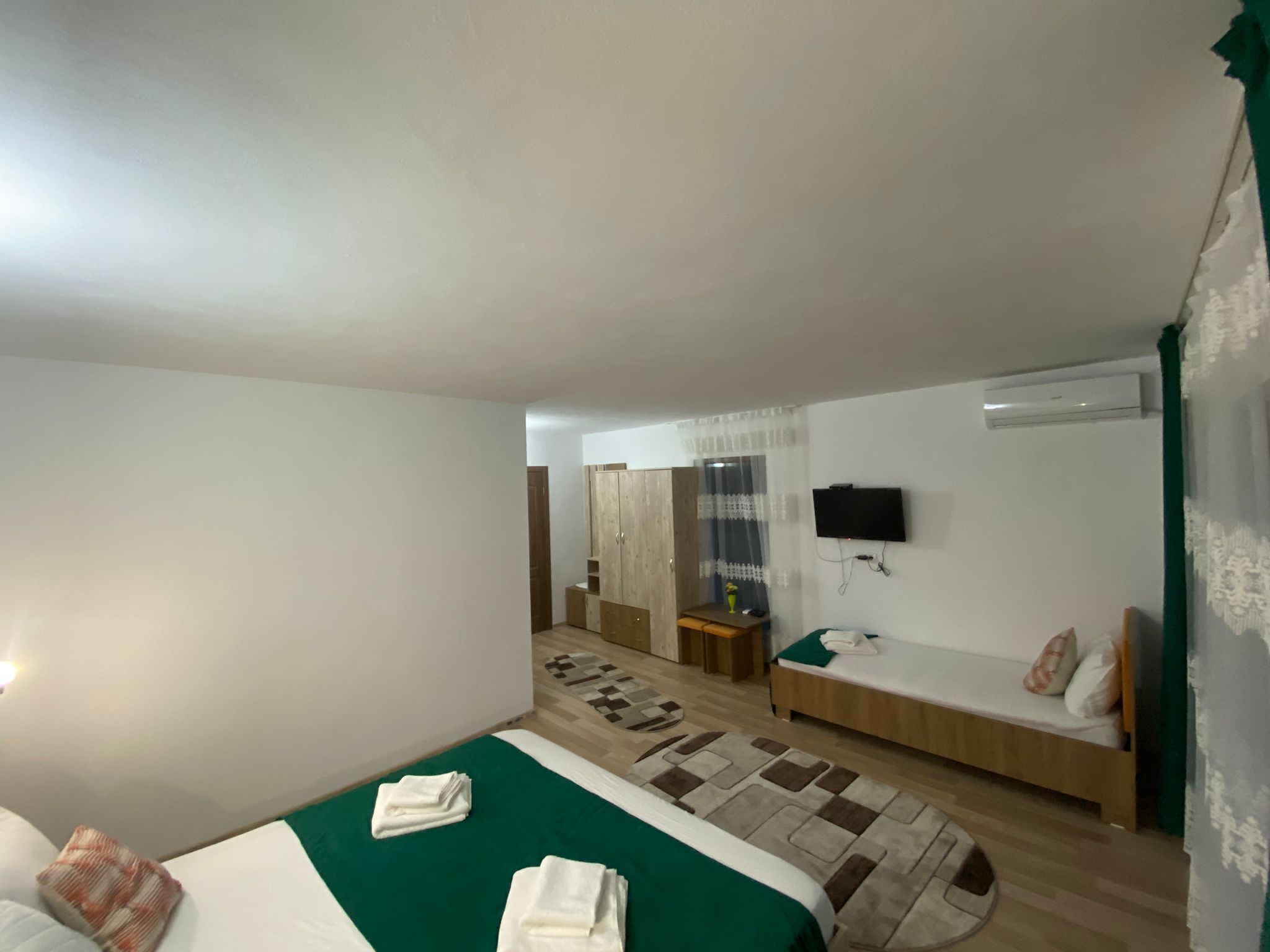A hotel room with two beds, a TV mounted on the wall, and a small desk with a chair.