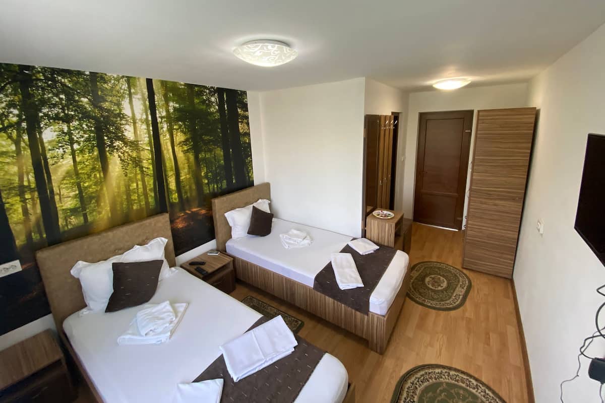 A hotel room with two beds, a large forest mural, a mirror, and a TV.