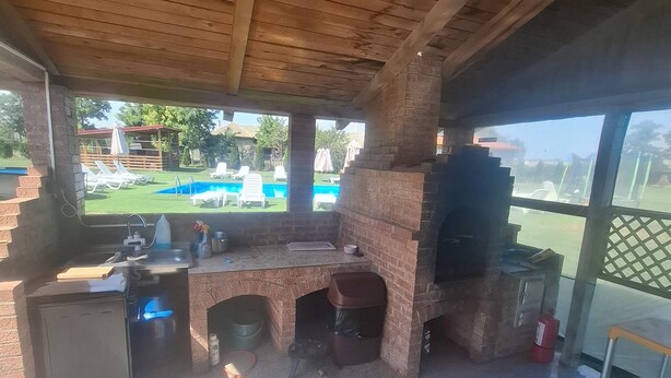 A covered outdoor area with a brick barbecue, a pool, and lounge chairs. - Paradiso Resort (Murighiol)