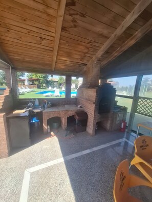 A covered outdoor area with a brick barbecue, a pool, and lounge chairs. - Paradiso Resort (Murighiol)