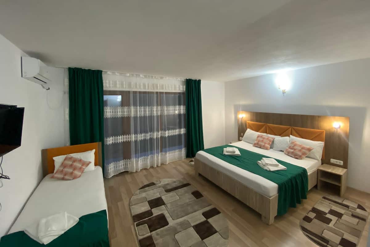 A hotel room with a bed, a smaller bed, a desk, a chair, a TV, and a window with curtains.