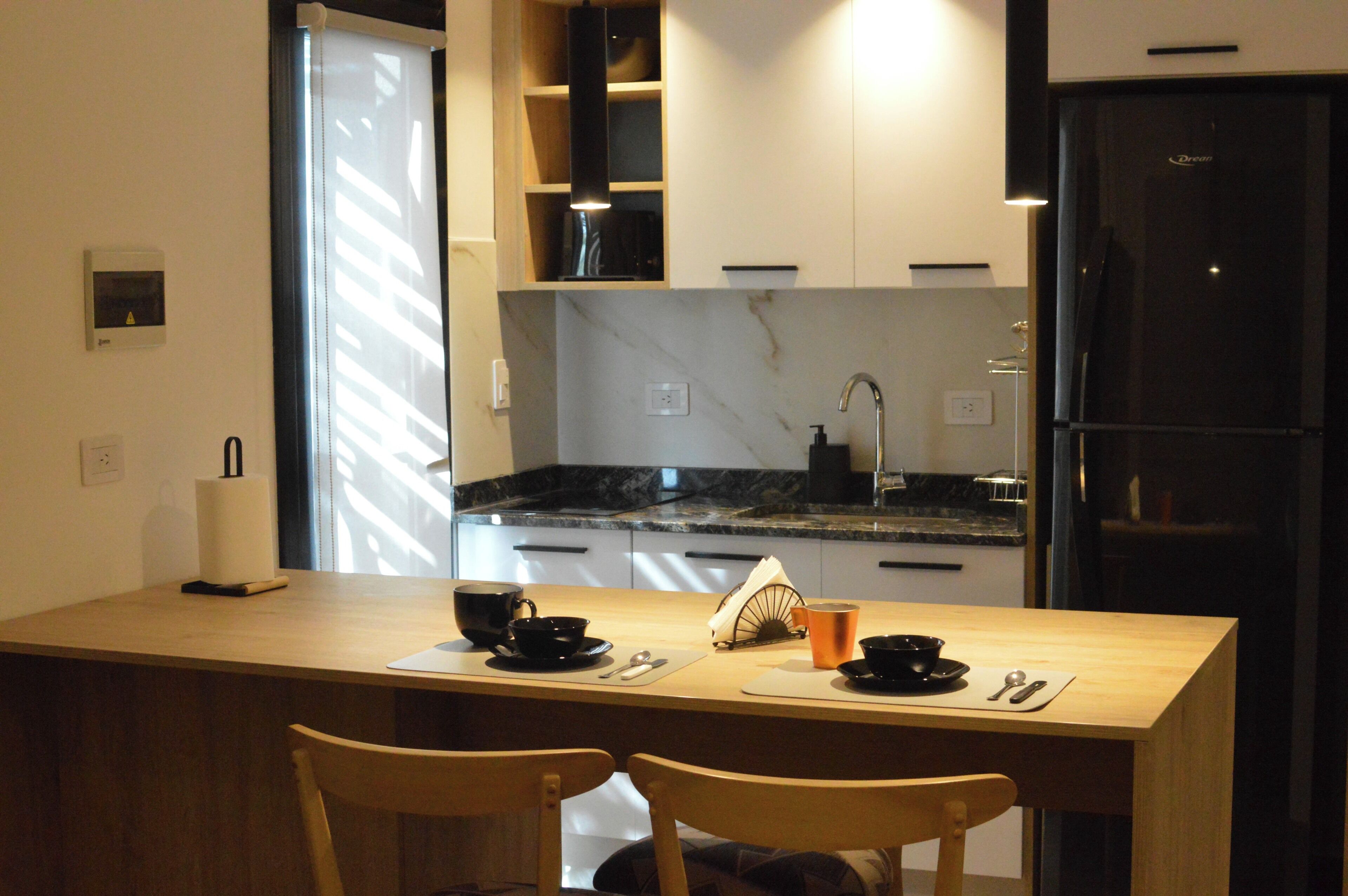 A compact kitchen with a dining area, including a wooden table, chairs, and a refrigerator.
