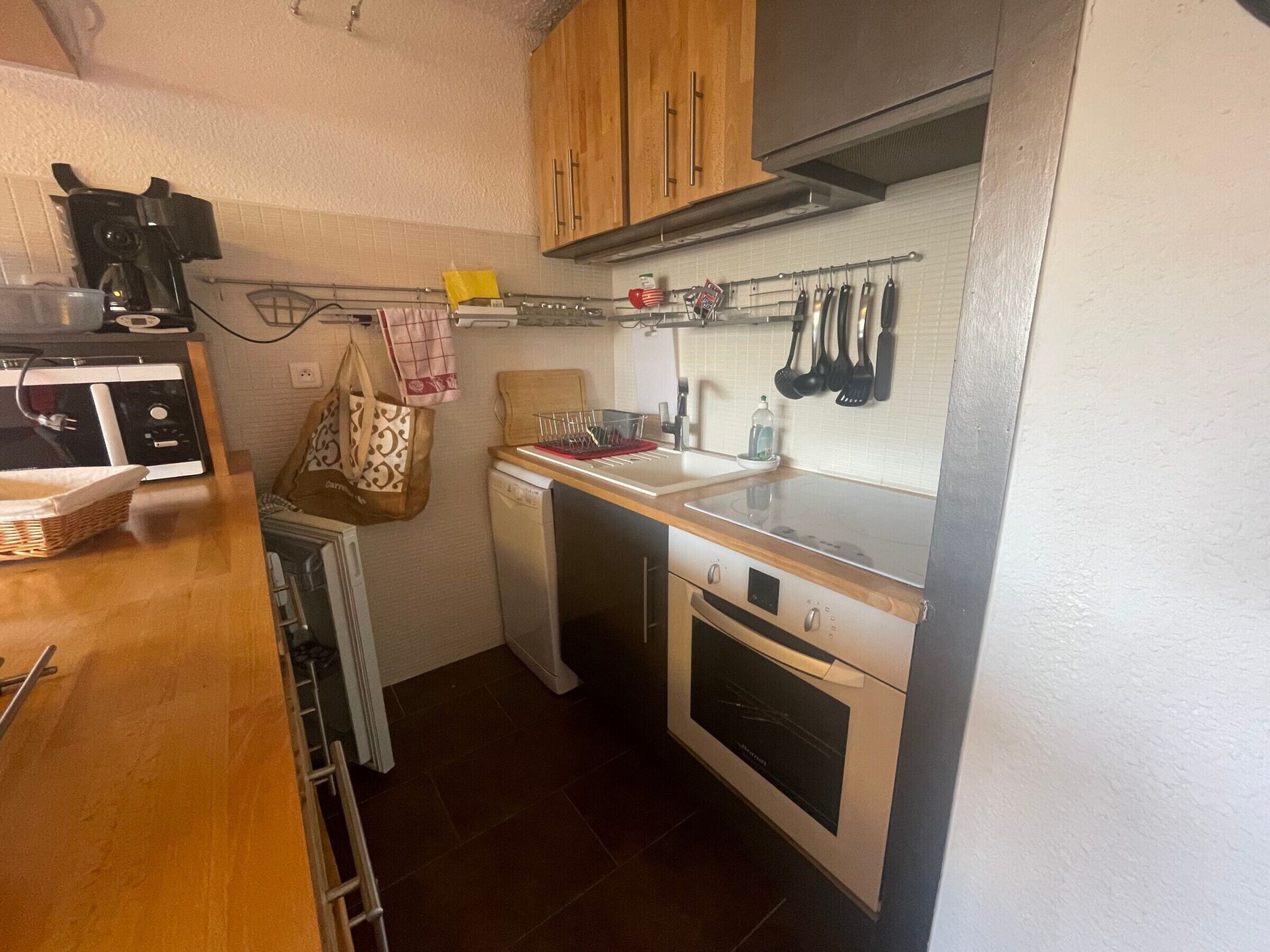 Una cuina compacta amb armaris de fusta, un rentaplats, un forn i una cafetera.
