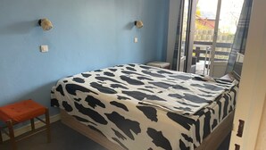 A bedroom with a bed, a small orange stool, and a window with a view of the outside. - Pra-Loup 1600 - T2 Apartment for 6, central location, near slopes (Pra-Loup)