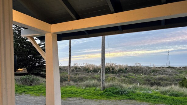 A covered outdoor area with a view of a grassy field and a distant power line tower. - Oceanview Retreat — 2BR, Walk to the Beach (Samoa)