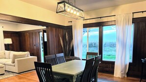 A dining area with a wooden table and chairs, a chandelier, and large windows with curtains. - Oceanview Retreat — 2BR, Walk to the Beach (Samoa)
