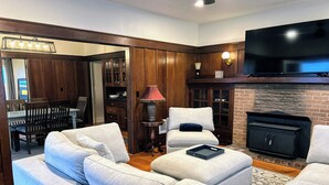 A living room with a sectional sofa, a fireplace, a television, and wooden paneling. - Oceanview Retreat — 2BR, Walk to the Beach (Samoa)