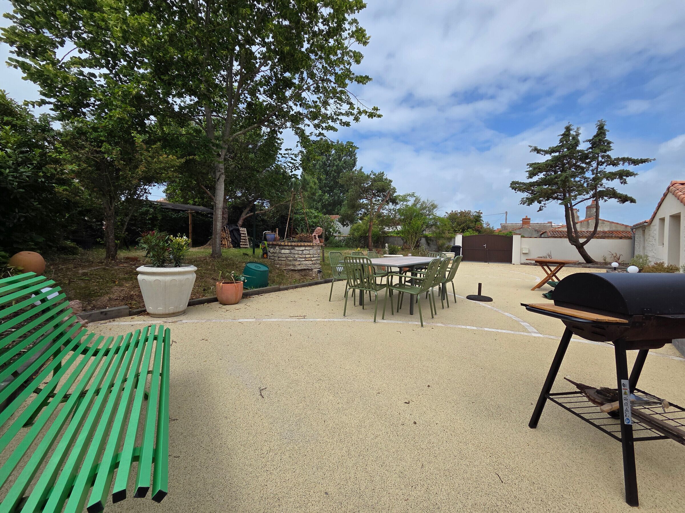 Un patio exterior con una parrilla, sillas verdes y una mesa.