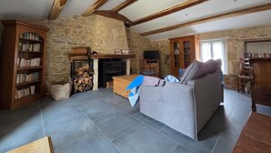 Ein rustikales Wohnzimmer mit freiliegenden Holzbalken, einer Steinwand, einem Kamin, einem Sofa und einem Bücherregal.
