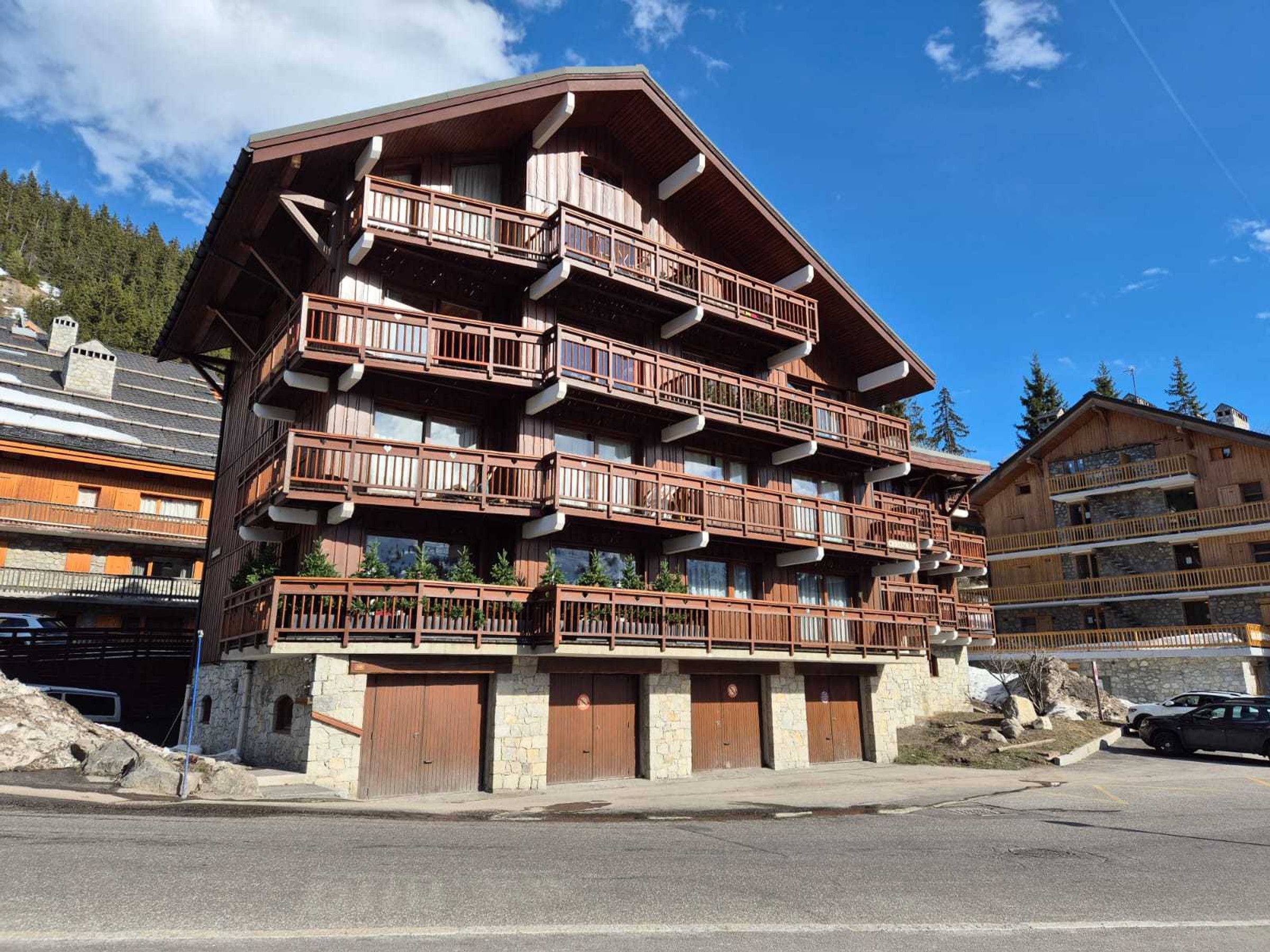 A multi-story wooden building with balconies, stone walls, and a parking area.