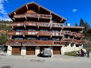 Ein mehrstöckiges Holzgebäude mit Balkonen, steinernen Untergeschossen und einem Parkplatz mit einem Auto.