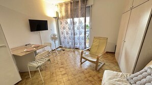A compact room with a bed, a desk with a chair, a TV, and a fan.