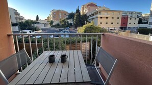 A balcony with a wooden table and two chairs, overlooking a parking area and buildings.