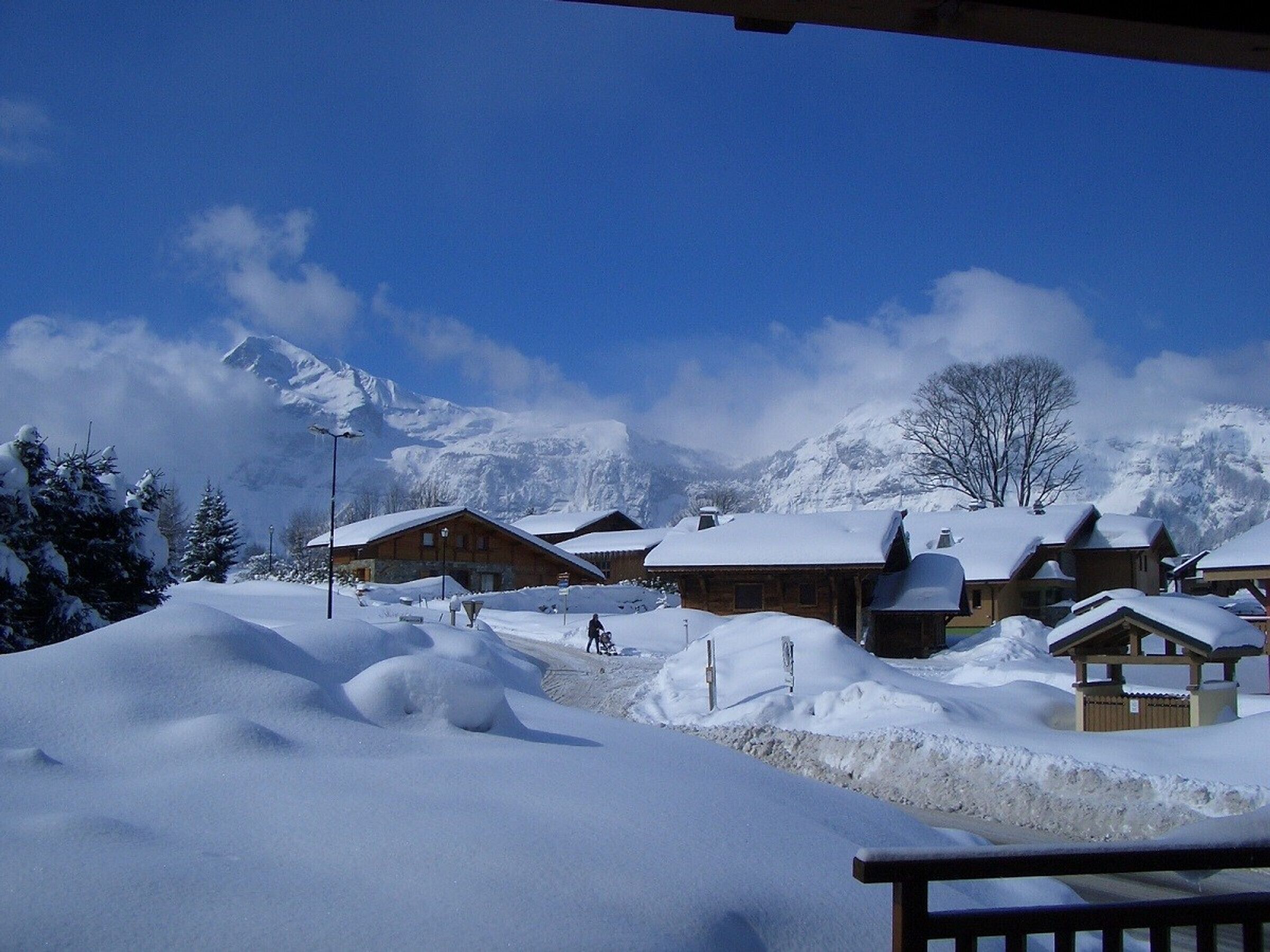 A snow-covered village with wooden buildings, a clear sky, and mountains in the background.