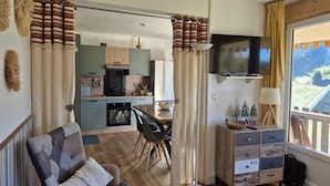 Espaço compacto com sofá, mesa de jantar, cozinha e televisão.