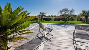 Eine Holzterrasse mit Pool, umgeben von üppiger Vegetation und wolkenlosem, blauem Himmel.
