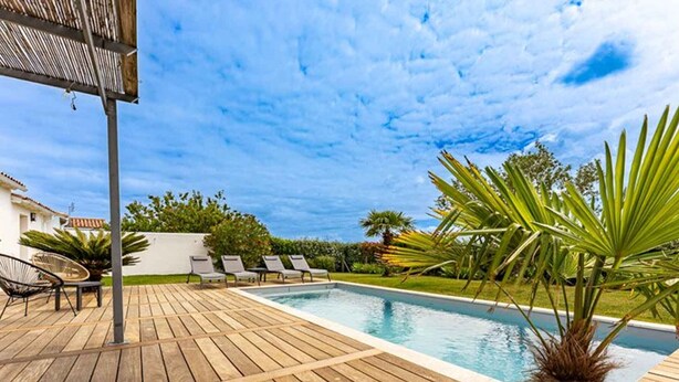 Eine Holzterrasse mit Pool, Liegestühlen und einer Palme.
