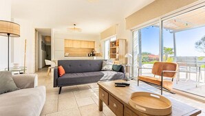 Ein modernes Wohnzimmer mit einem grauen Sofa, einem Holztisch und einem großen Fenster mit Blick ins Freie.