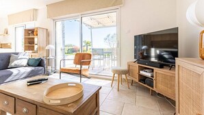 Ein modernes Wohnzimmer mit Sofa, Couchtisch, Fernseher und einer Schiebeglastür, die zu einem Außenbereich führt.
