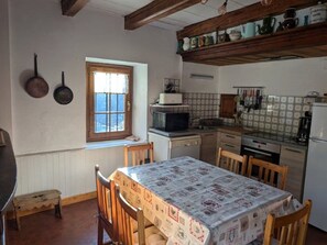 Eine kleine Küche mit Esstisch, Holzstühlen, einem Fenster und verschiedenen Küchengeräten.