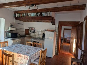 Eine rustikale Küche mit Holzbalken, einem Esstisch mit gemustertem Tischläufer und einem Kühlschrank.