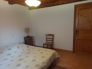 Ein Schlafzimmer mit einem Bett, einem Sessel, einem Nachttisch und einer Holztür.