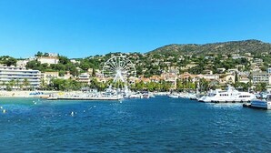 Una cittadina costiera con una ruota panoramica imponente, un porto turistico pieno di barche e palazzi lungo la riva.