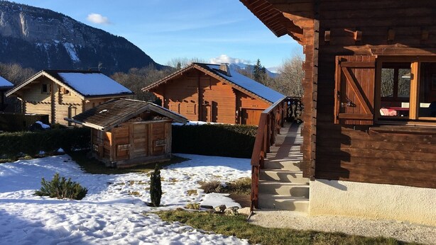 Una cabaña de madera con suelo cubierto de nieve, una construcción de madera pequeña y una montaña al fondo.