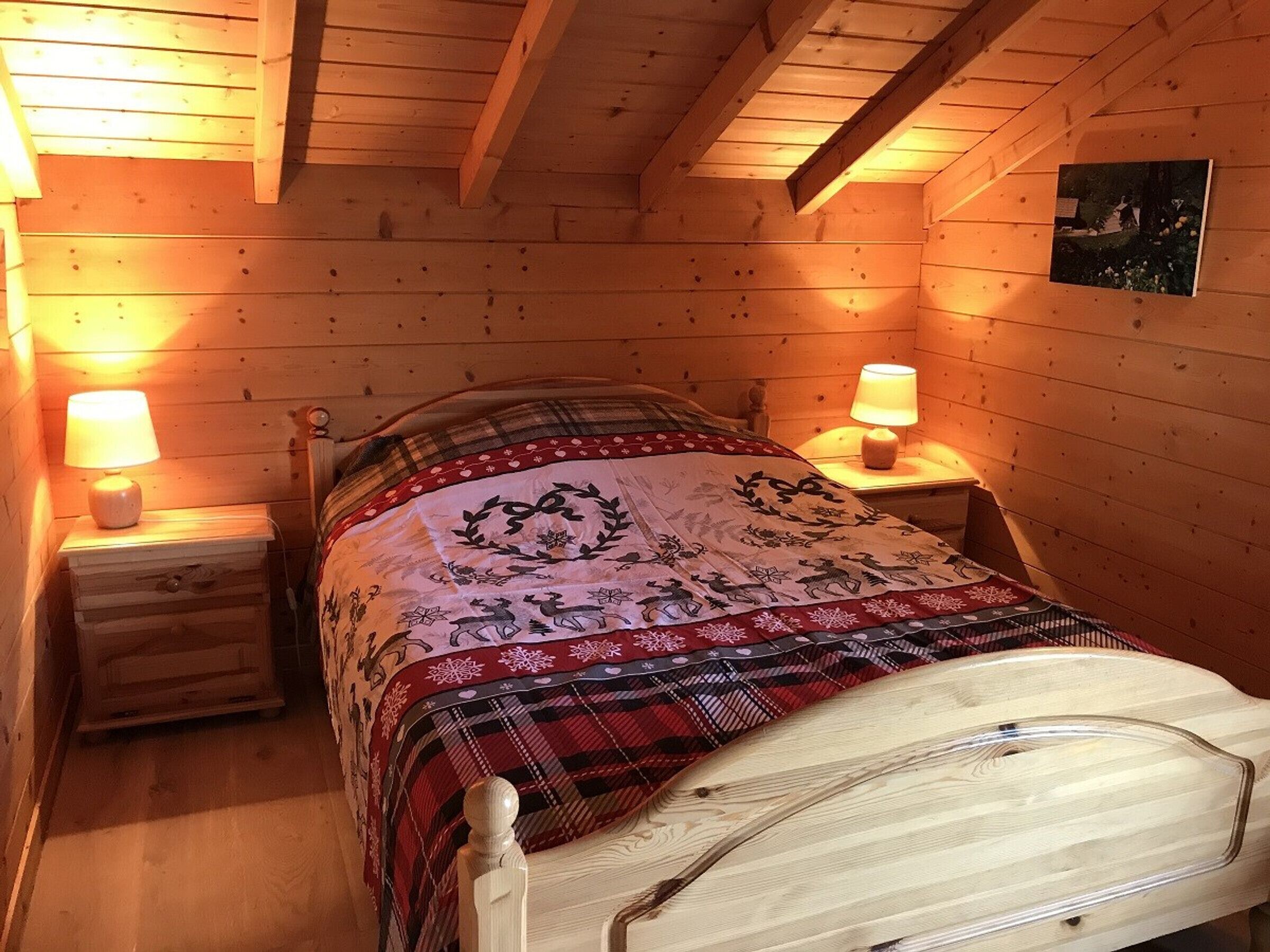 A cozy wooden cabin bedroom with a bed, two bedside lamps, and a framed picture on the wall.