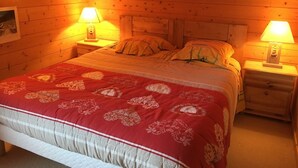 Una habitación acogedora de madera con una cama grande, dos mesitas de noche con lámparas, y un cuadro en la pared.