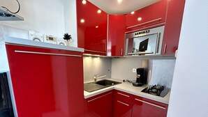 Uma cozinha compacta com armários vermelhos, micro-ondas de aço inoxidável, cafeteira e pia.