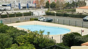 Piscina rodeada por vegetação, estacionamento e marina com barcos.