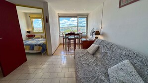 Um quarto com cama, sofá, mesa de jantar com cadeiras, ventilador e janela com vista.