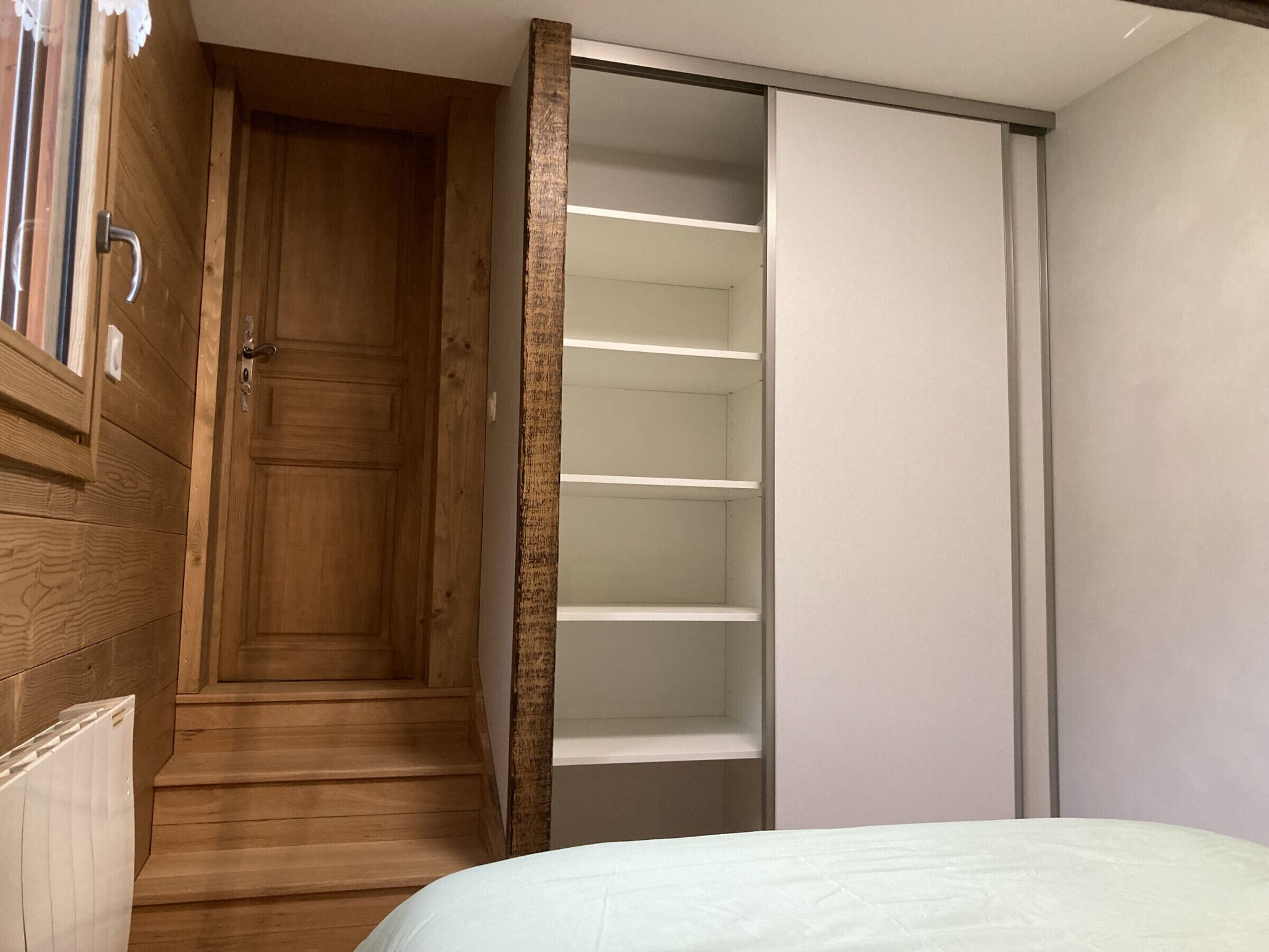 A bedroom with a wooden door, a white bed, and a closet with shelves.