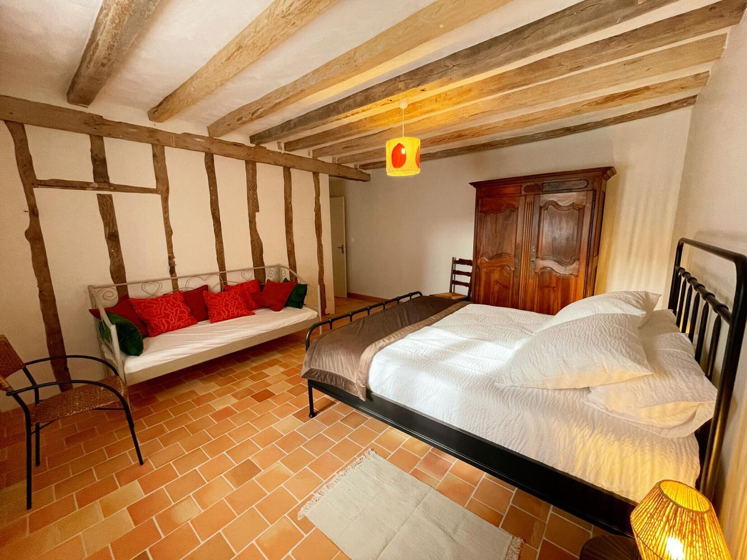 A bedroom with a bed, a wooden wardrobe, a bench, and a hanging light fixture.