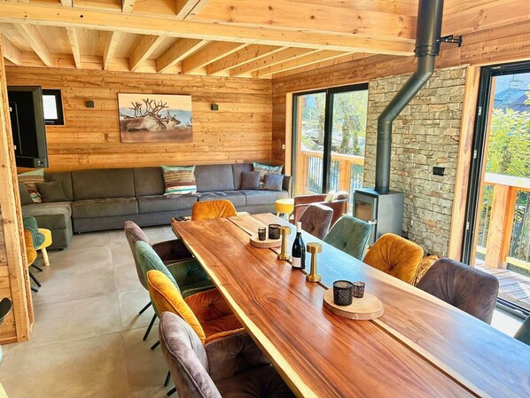 Interior moderno de cabaña de troncos con comedor, sofá y chimenea de piedra.